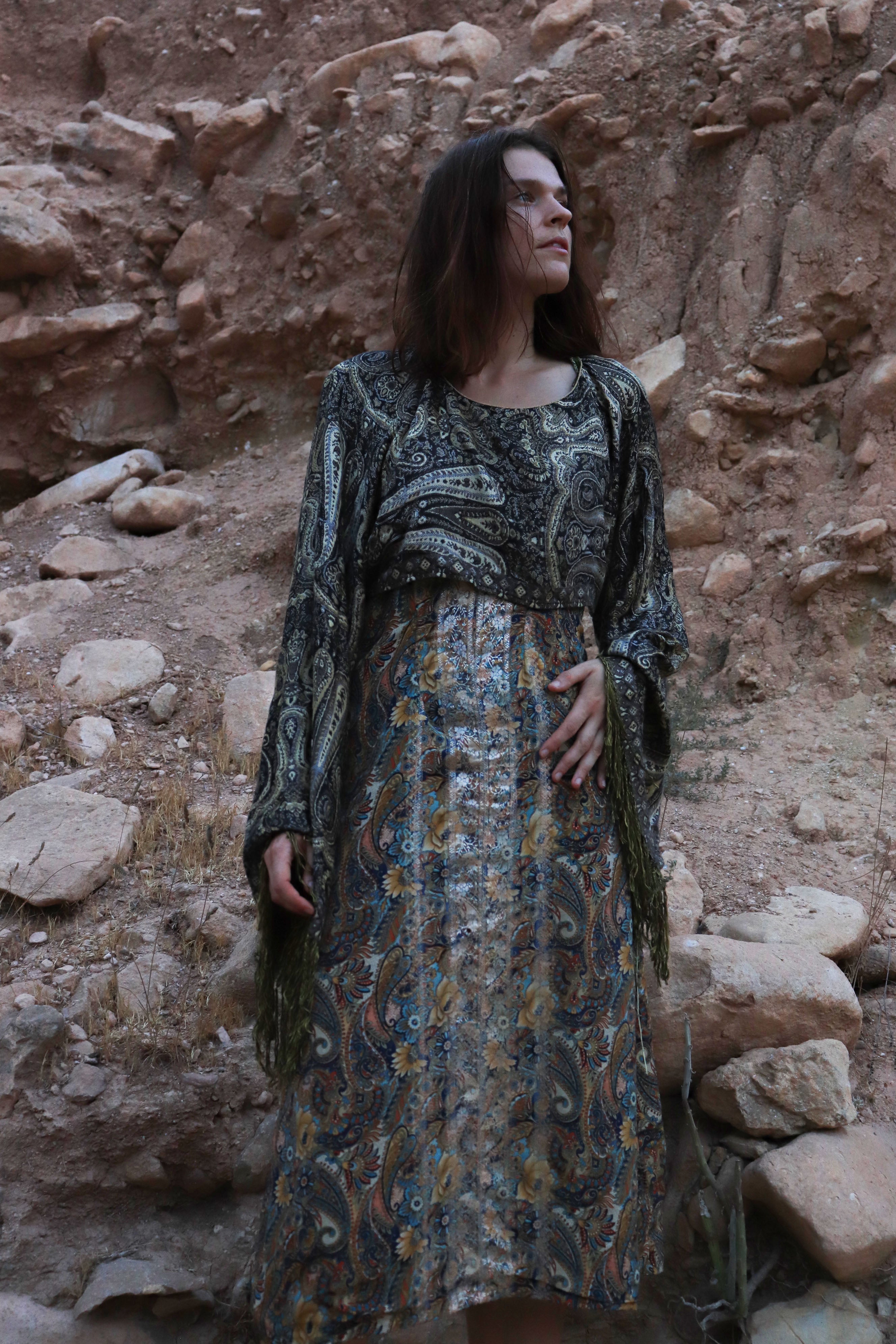 Woman in a patterned dress standing against a rocky wall