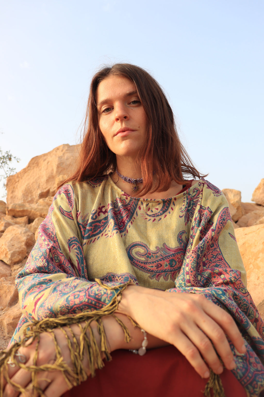 Woman wearing a colorful patterned dress sitting against a rocky landscape with a clear blue sky.