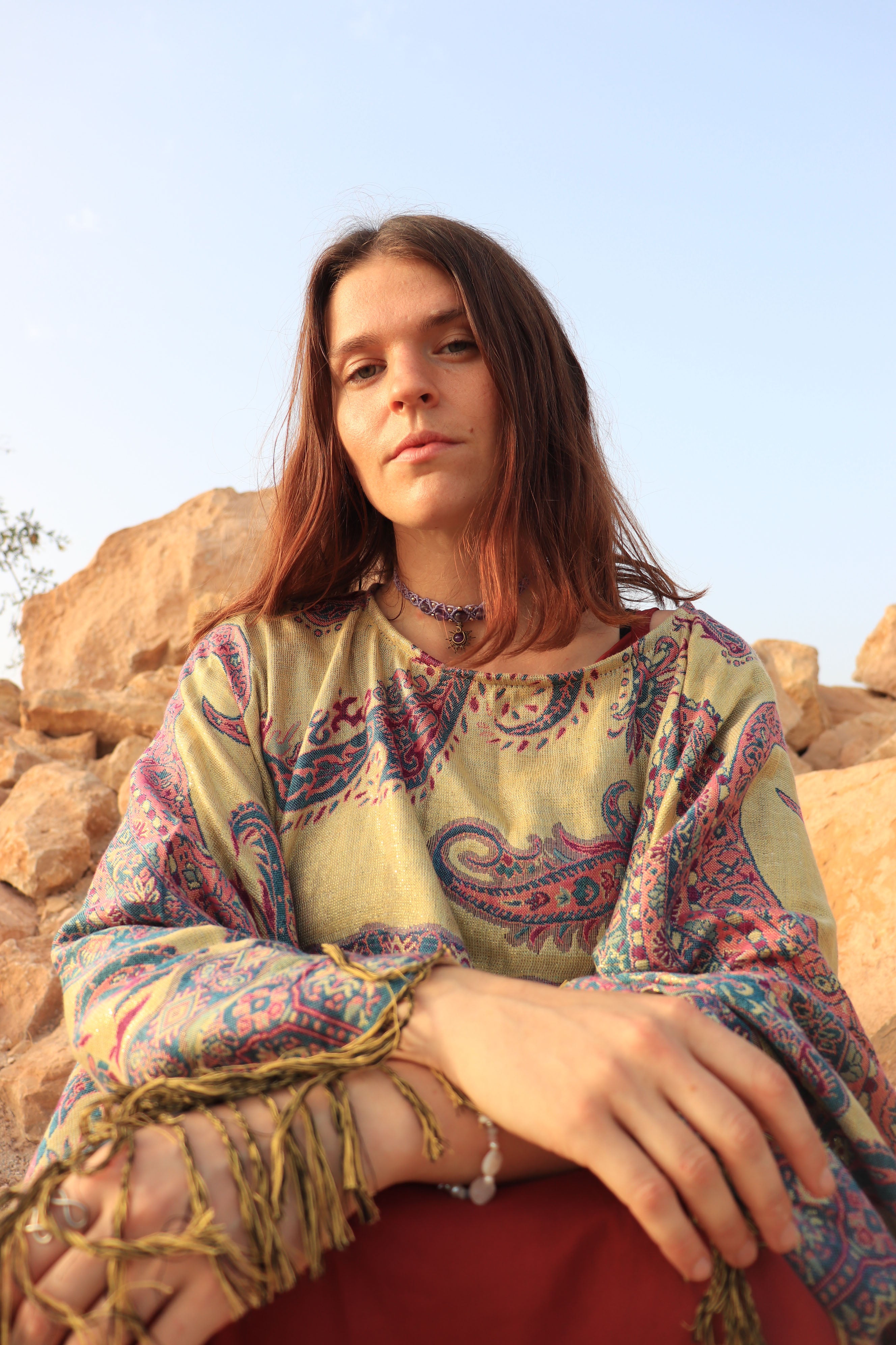 Woman wearing a colorful patterned dress sitting against a rocky landscape with a clear blue sky.
