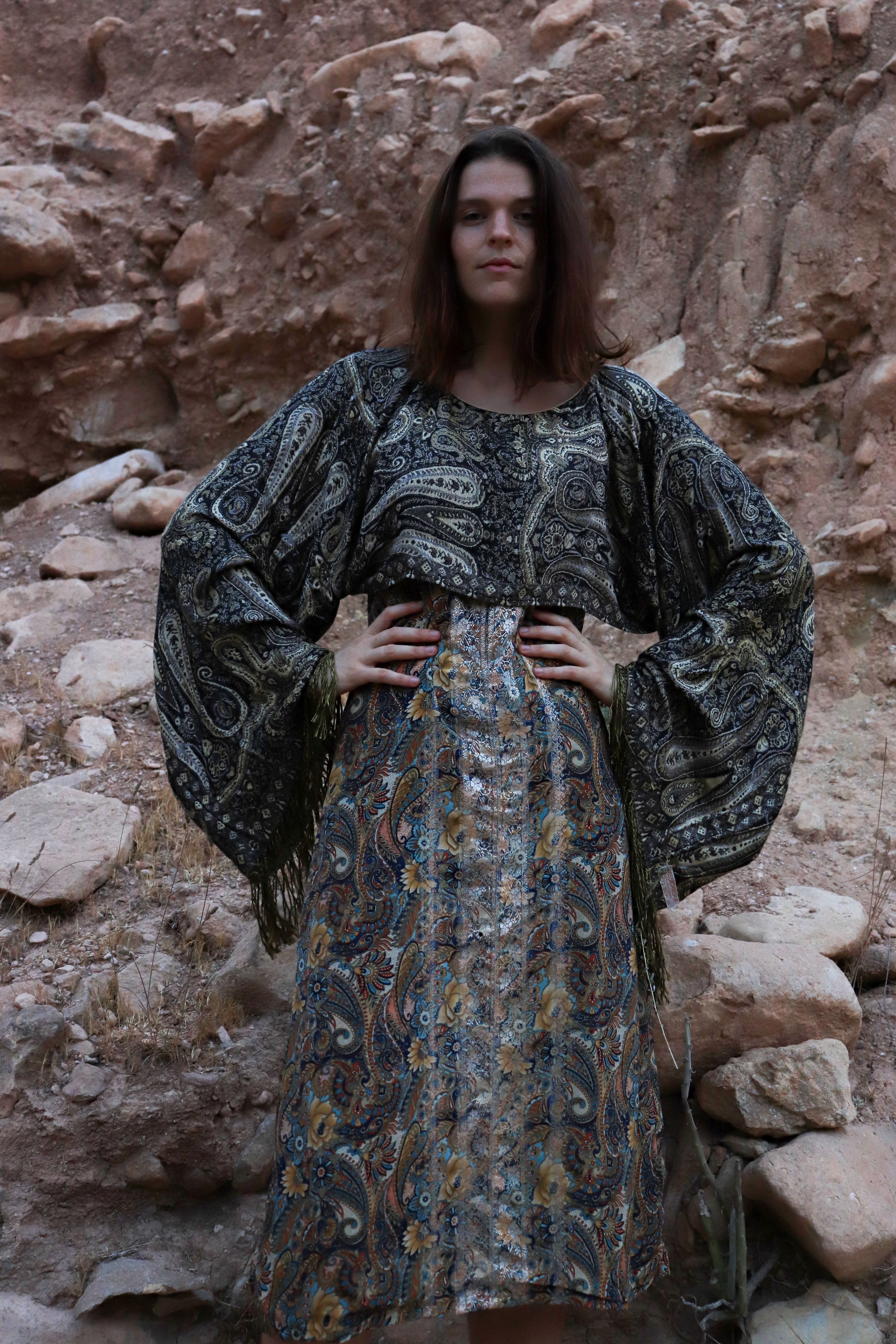 Woman wearing a patterned dress standing against a rocky wall.