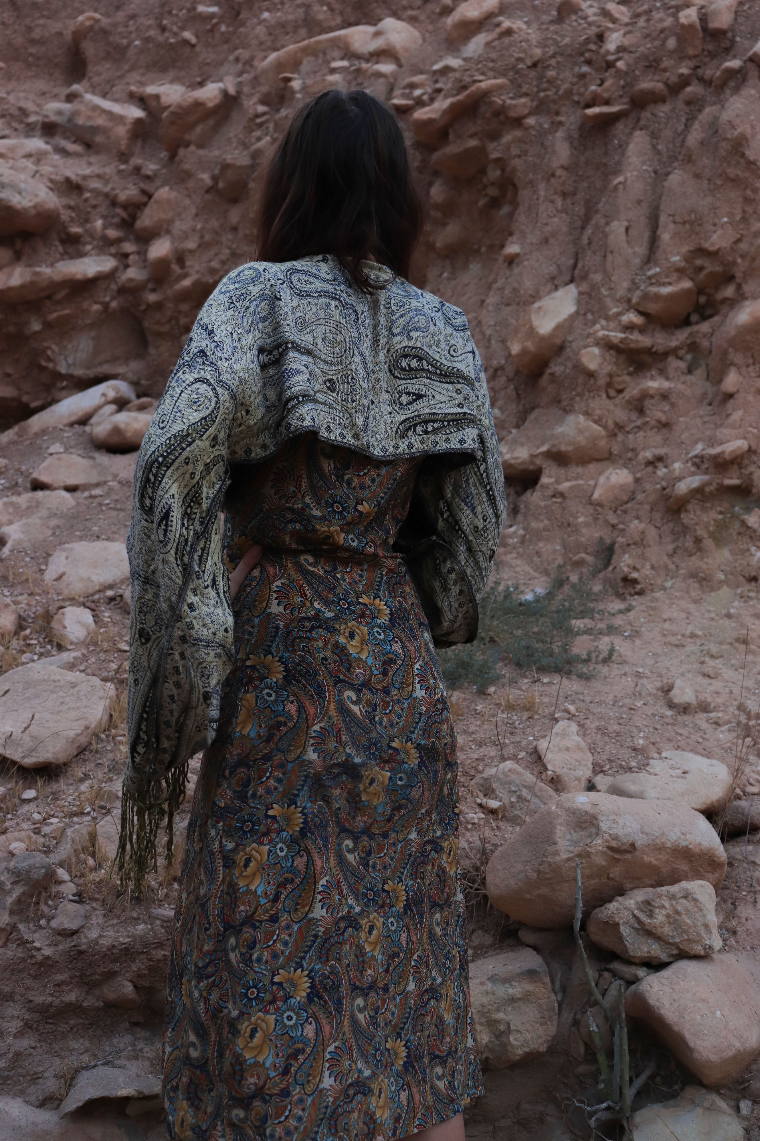 Person wearing a patterned dress and shawl standing in a rocky desert landscape
