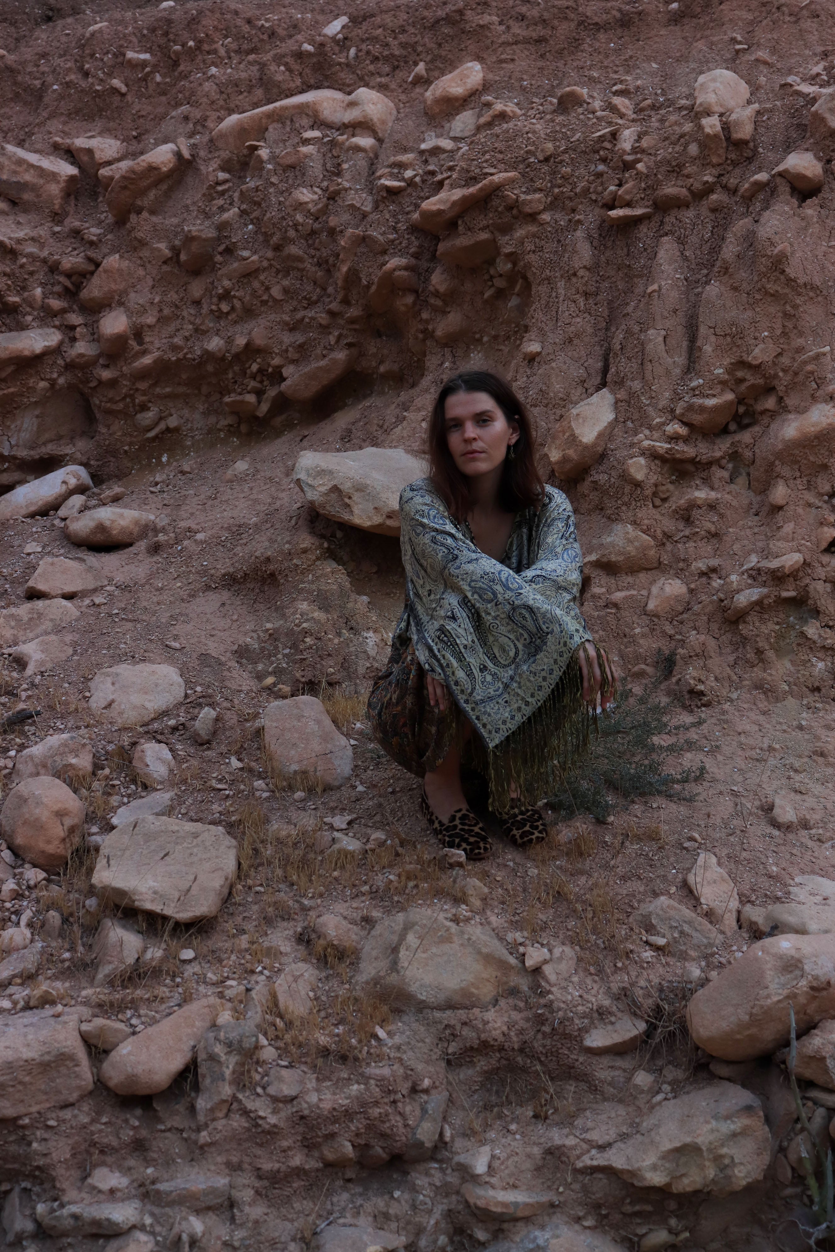 Woman sitting on a rocky surface wearing a patterned shawl.